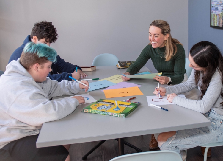 3 students and 1 teacher sitting at a table. The students are drawing.