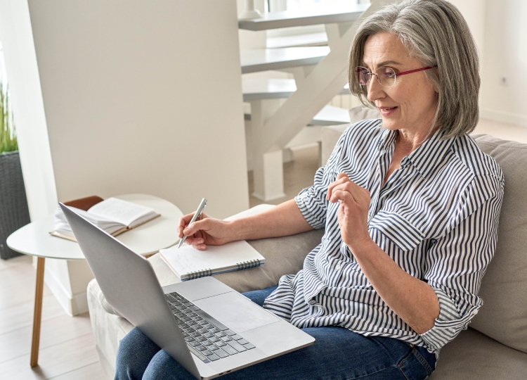Woman over 50 looking at computer and taking written notes